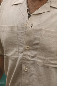 Close-up of a man wearing a light beige linen short-sleeve button-up shirt with two chest pockets and cream-colored buttons.