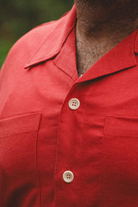 Close-up of a person wearing a red short-sleeve camp-collar button-up shirt with cream-colored buttons.