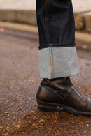 Cuffed dark raw denim jeans paired with brown leather ankle boots on gravel surface