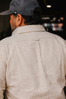Man wearing cream flannel Oxford shirt with back yoke and center pleat, paired with dark cap