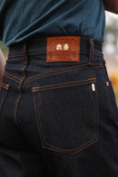 Close-up of dark indigo Kaisen Denim jeans with a brown leather patch and orange stitching