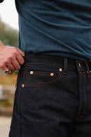 Close-up of a person wearing dark indigo raw denim jeans with contrast orange stitching and a teal shirt