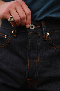 Close-up of hand with skull ring fastening button on dark indigo raw denim jeans with orange stitching