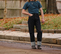 Person wearing dark indigo wide straight jeans with rolled cuffs, blue t-shirt, and leather boots outdoors