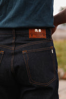 Close-up of indigo 16.5oz Kaisen denim wide straight jeans with orange stitching and leather patch detail