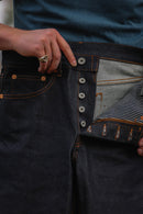 Close-up of hands showing button fly and interior striped lining of dark indigo wide straight jeans with orange stitching