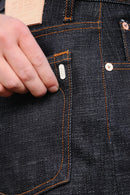 Close-up of hand touching dark indigo denim jeans pocket with orange stitching and metal rivets