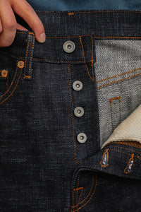 Close-up of hand holding dark indigo raw denim jeans with orange stitching and metal button fly